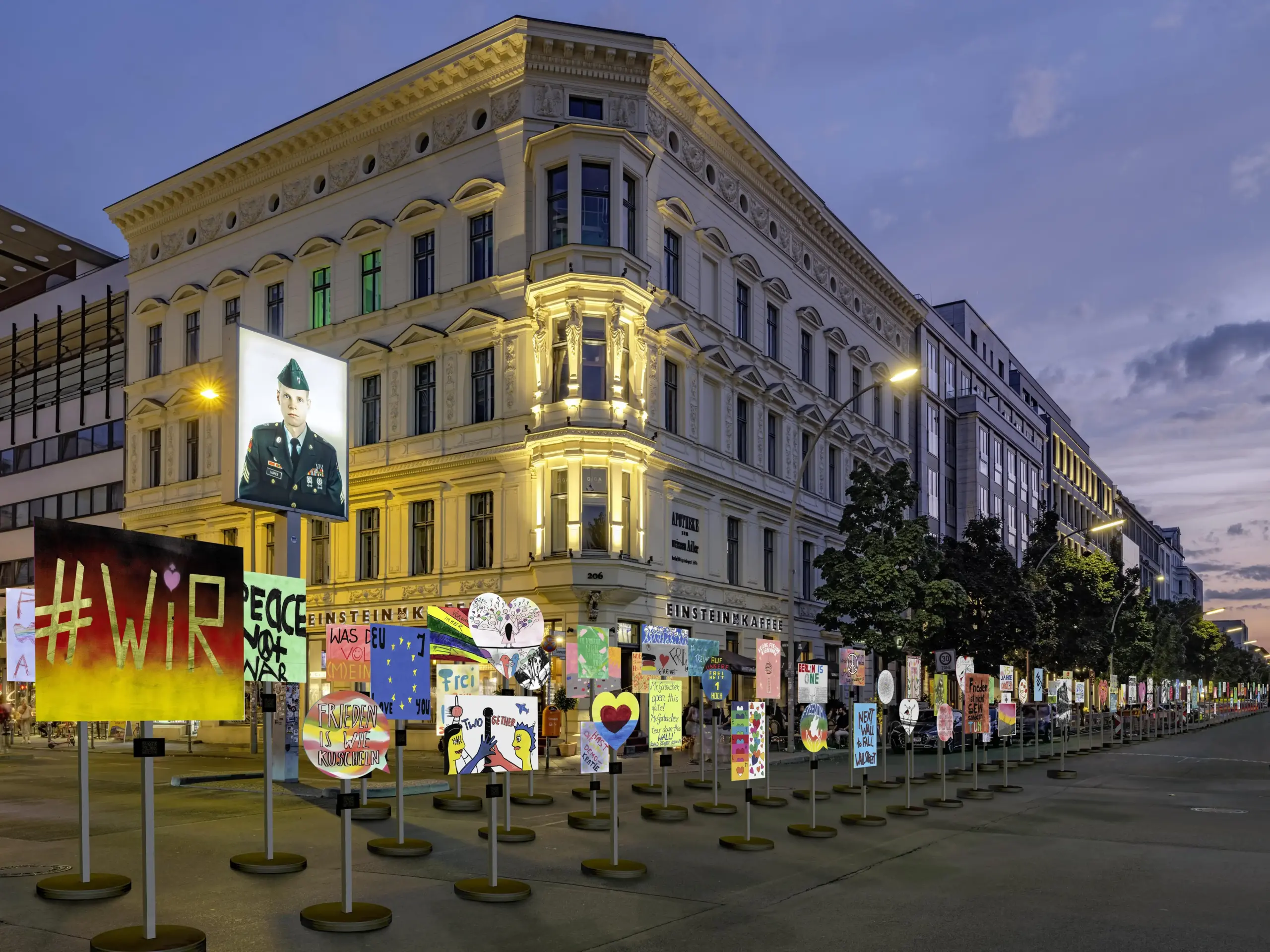 Visualisierung der Plakat-Installation im Berliner Stadtraum. Viele bunte Protestschilder stehen auf runden Füßen und Ständern in einer Reihe vor dem Checkpoint Charlie, am Kapelle-Ufer, der Zimmerstraße und in der Niederkirchner Straße.