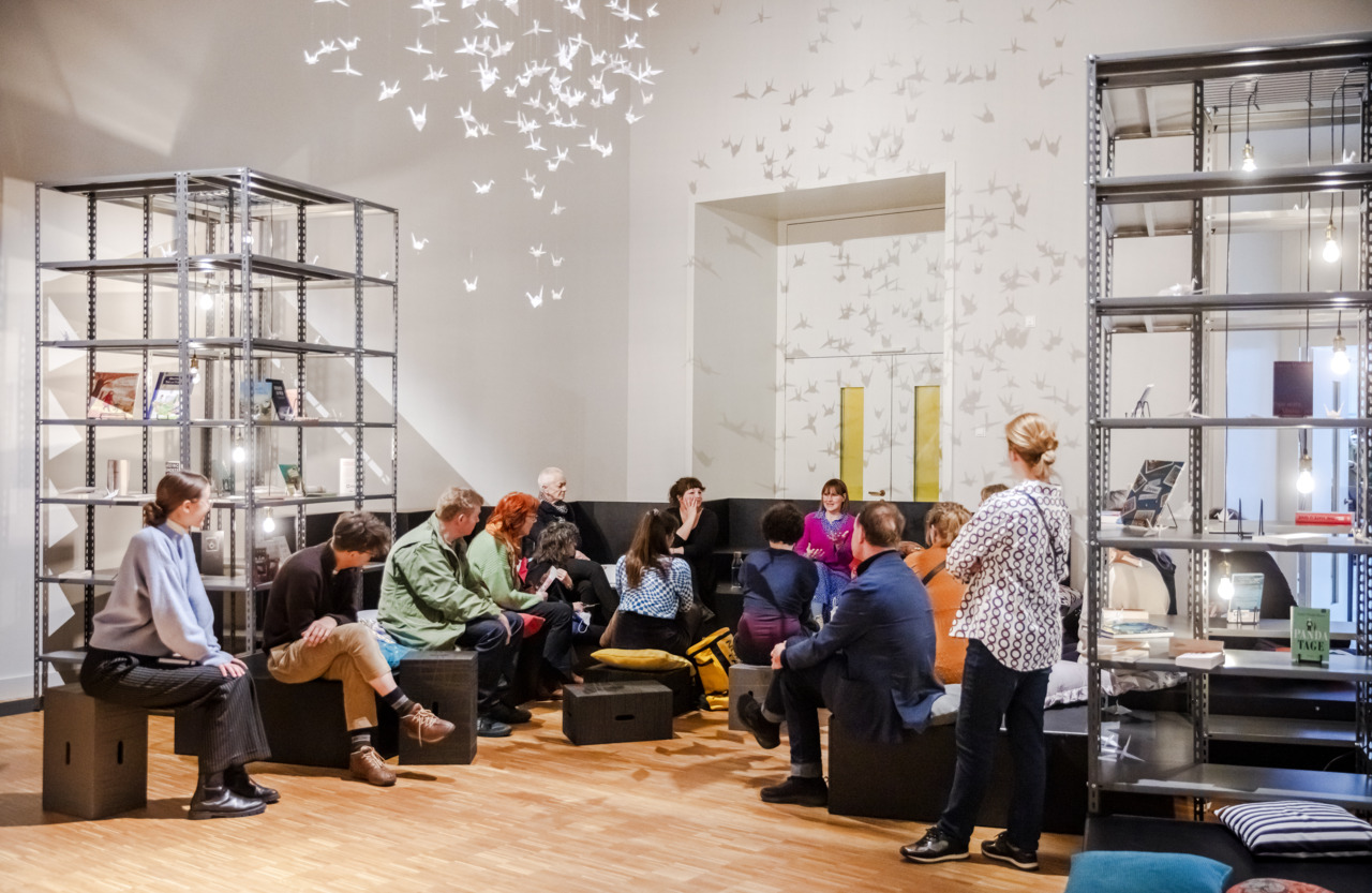 group of people sitting in a circle on sofas in exhibition space chatting