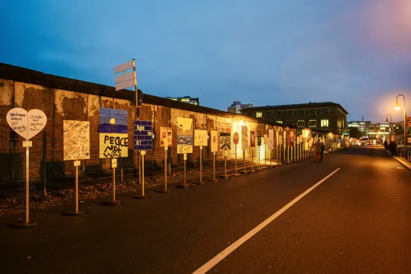 Schilder bei Nacht vor einem Mauerstreifen