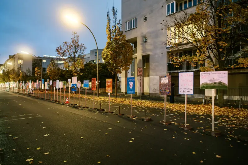 Bunte Schilder auf Straße mit Laub und Straßenlampen